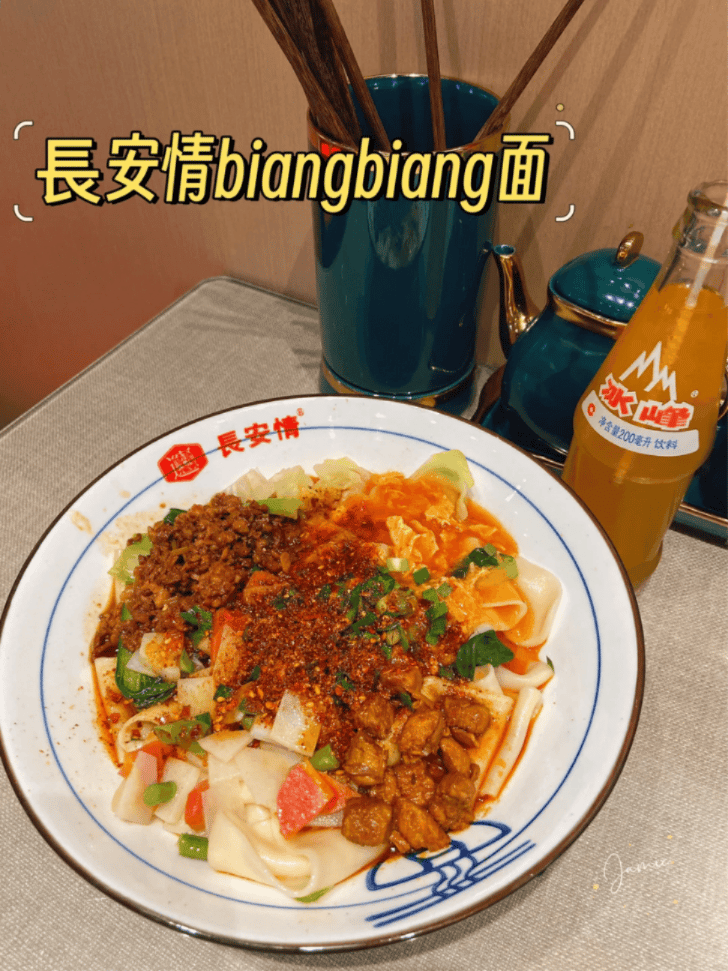 A plate of wide biang biang noodles topped with minced meat and vegetables