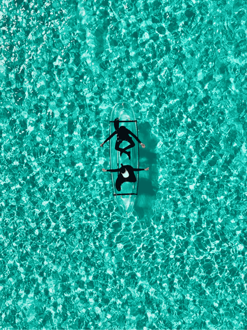 Overhead view of two people in a see-through kayak on bright turquoise water