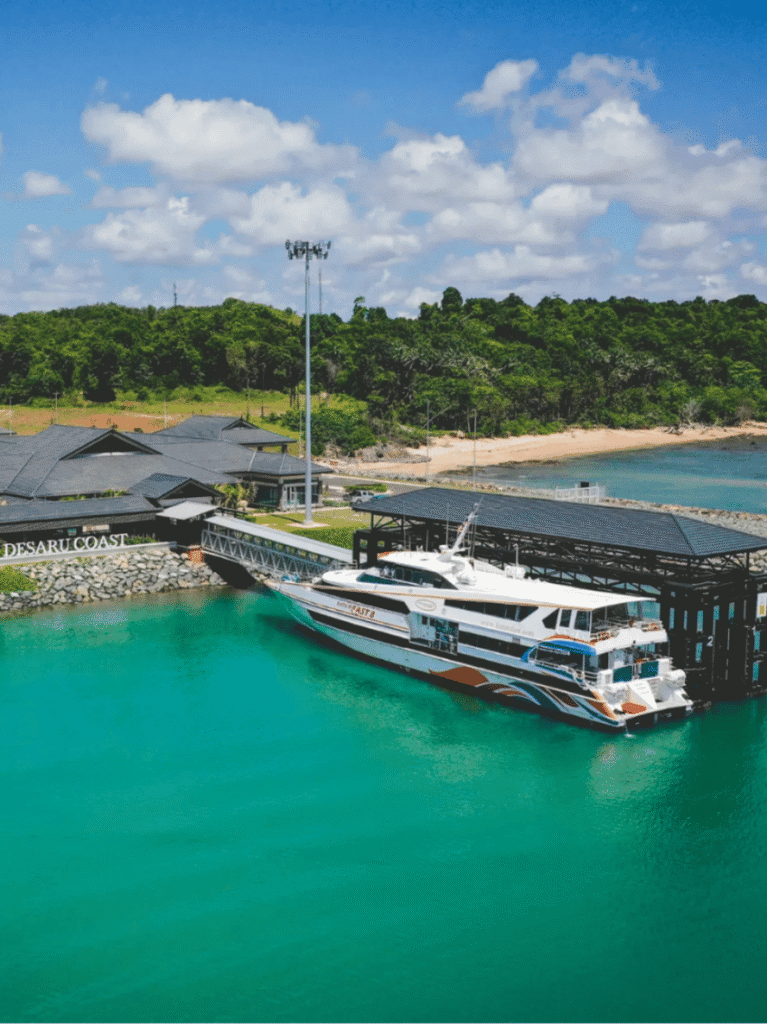 A passenger ferry berthed at a jetty beside turquoise water and green coastline at Desaru Coast
