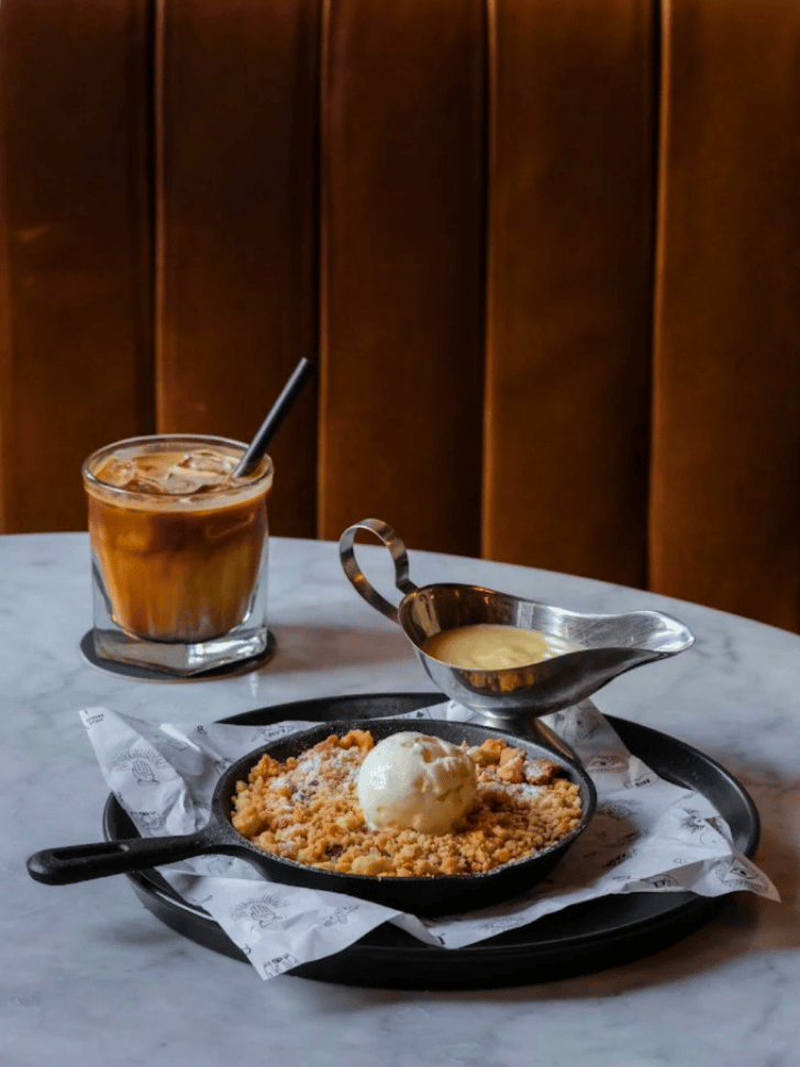 Skillet crumble with vanilla ice cream and an iced coffee on a marble table, Bali café