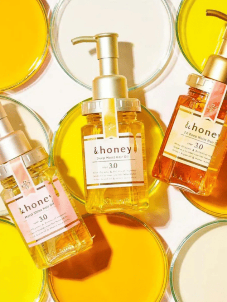 Three &honey hair oil bottles arranged on round glass dishes