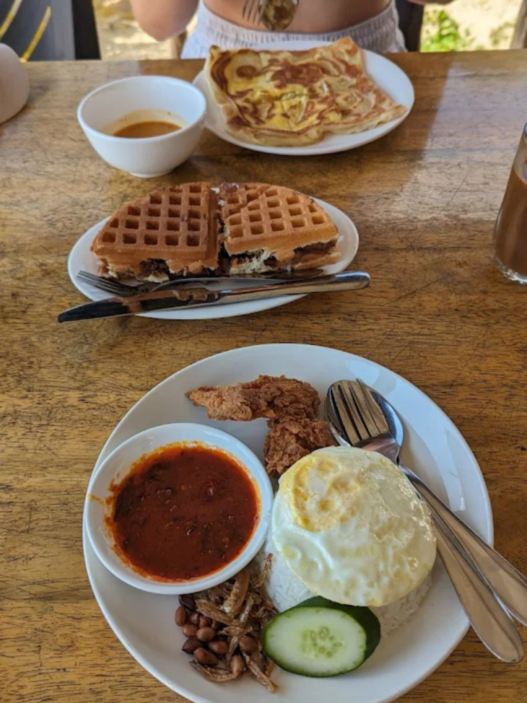 Plates of nasi lemak, waffles and roti with sambal on a cafe table