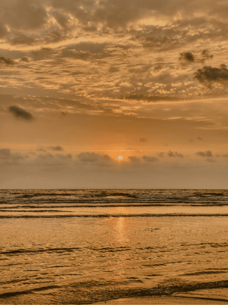 A golden sunset over Desaru beach, wet sand reflecting the sky as gentle waves roll in