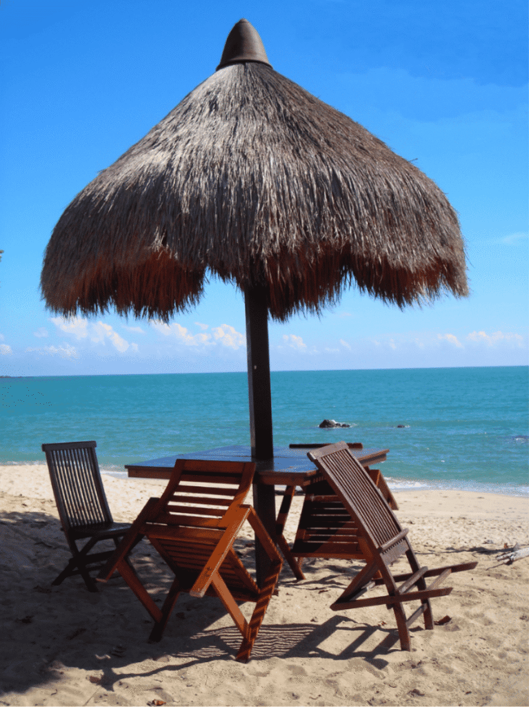 A thatched beach umbrella shading wooden loungers on Desaru's sandy shore by a turquoise sea