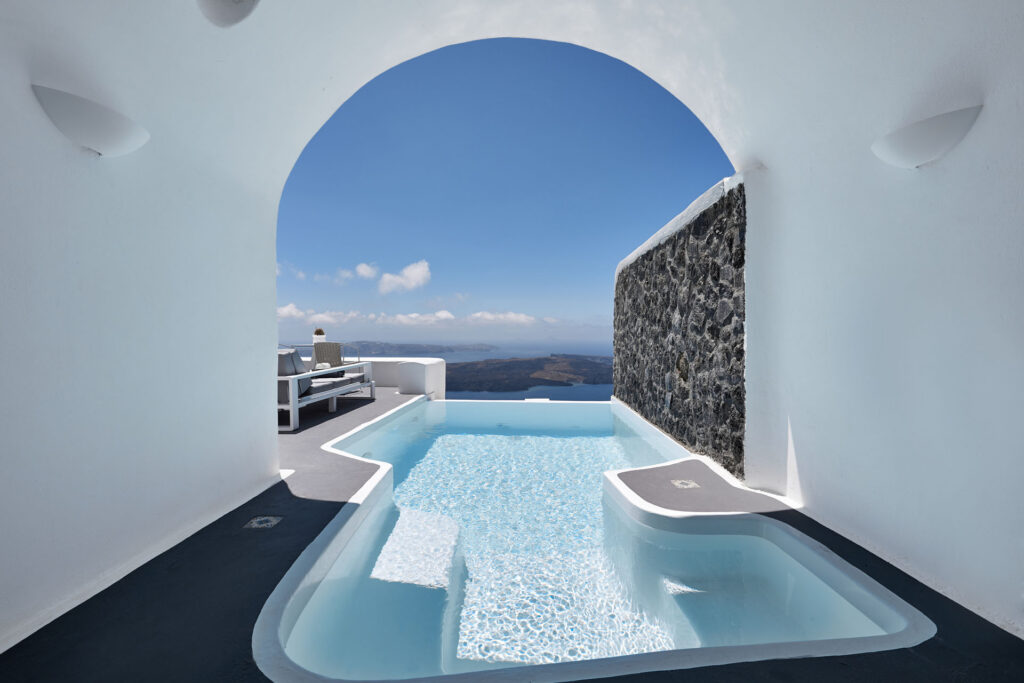 A cave-suite plunge pool framed by a white arch, looking out to the Santorini caldera