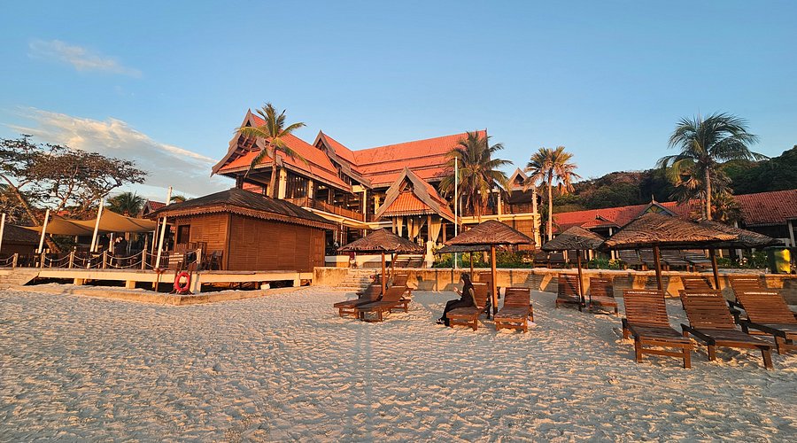 Malay-style beachfront resort with sun loungers and parasols on white sand at golden hour