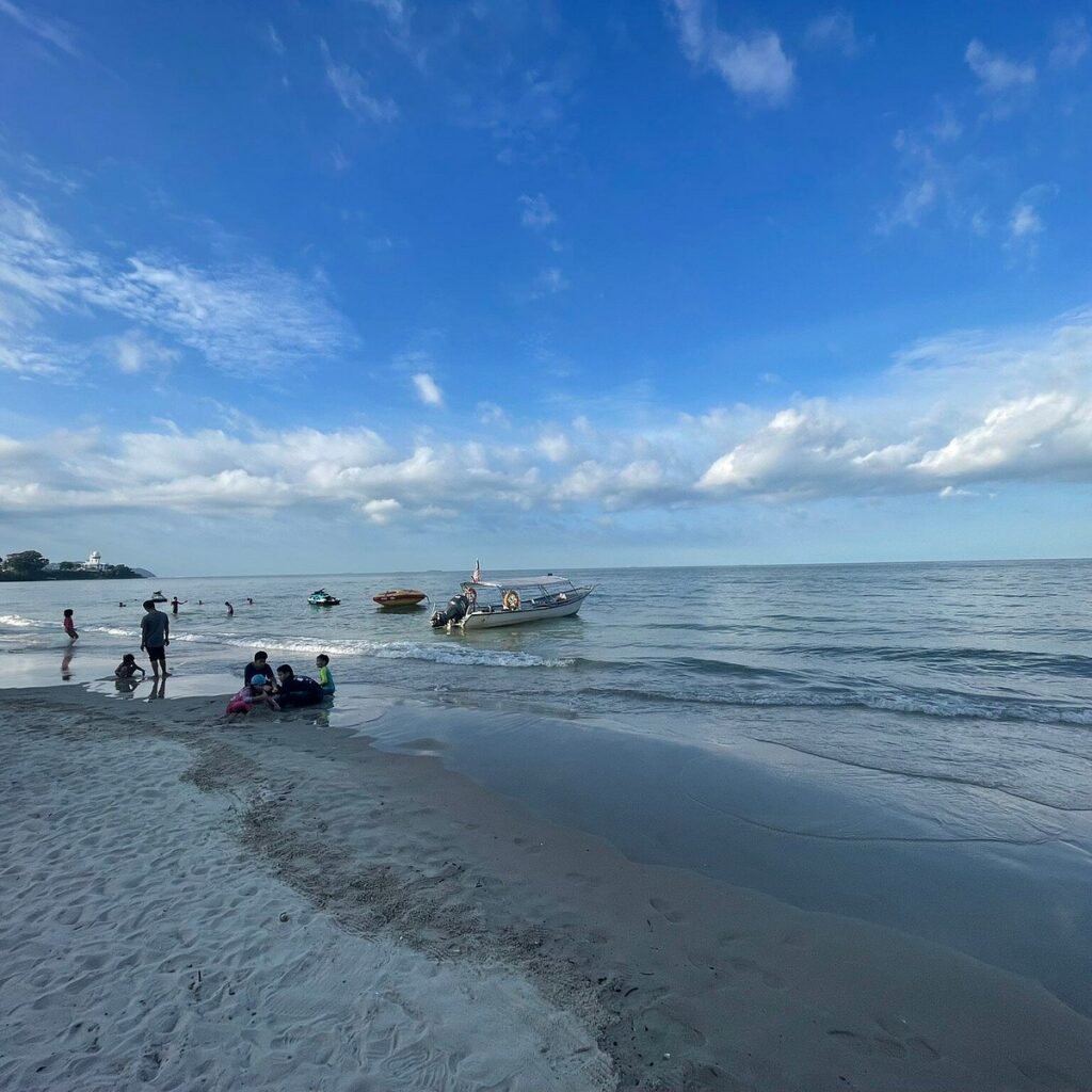 Families playing on Teluk Kemang beach with a boat and jet ski offshore