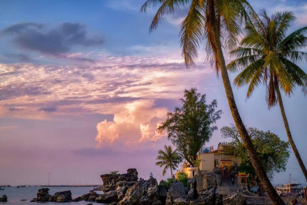 Dinh Cau shrine on a rocky outcrop by the sea under a pink sunset sky, framed by palms