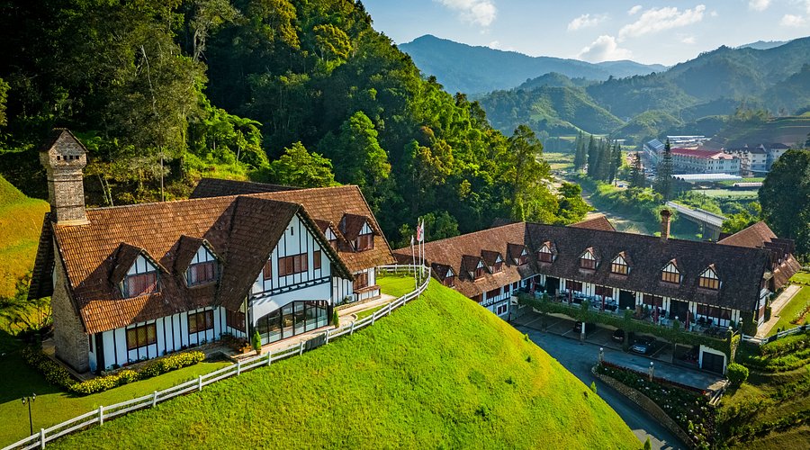 Aerial view of the Tudor-style Lakehouse hotel on a green hillside with mountains behind