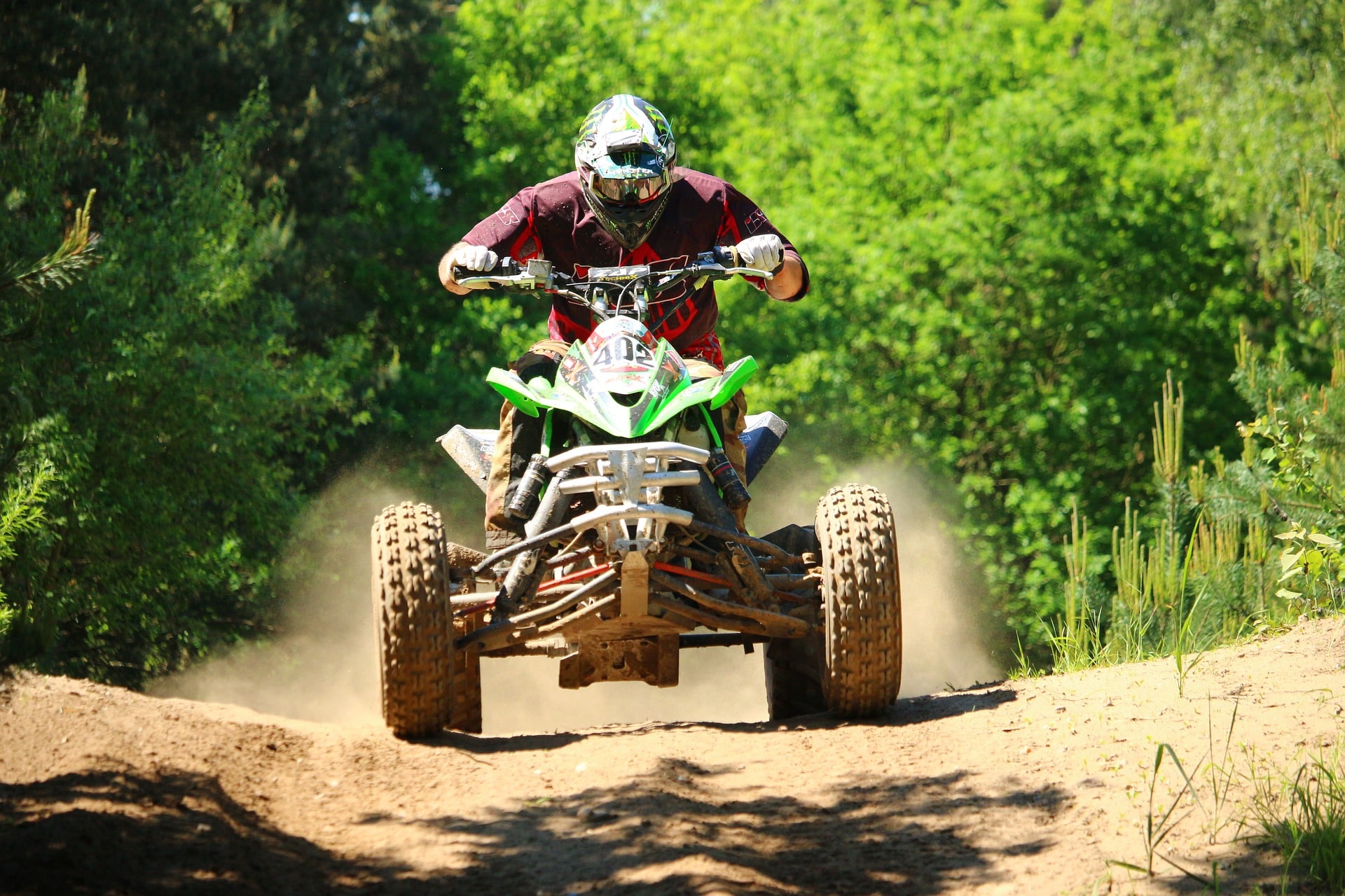 Rider on a quad bike kicking up dust along a forest dirt trail