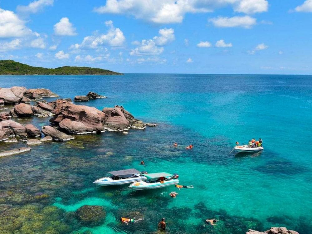 Snorkellers and speedboats in clear turquoise water by rocks in the An Thoi islands