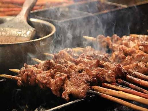 Cumin-dusted lamb skewers grilling over charcoal with rising smoke