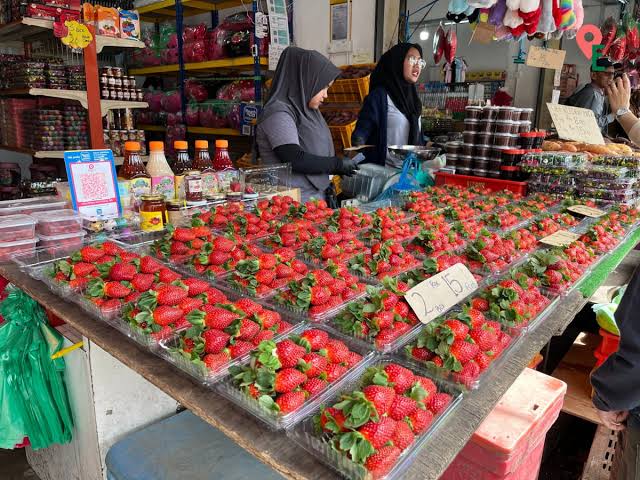 Punnets of red strawberries stacked at a stall with vendors at Kea Farm Market