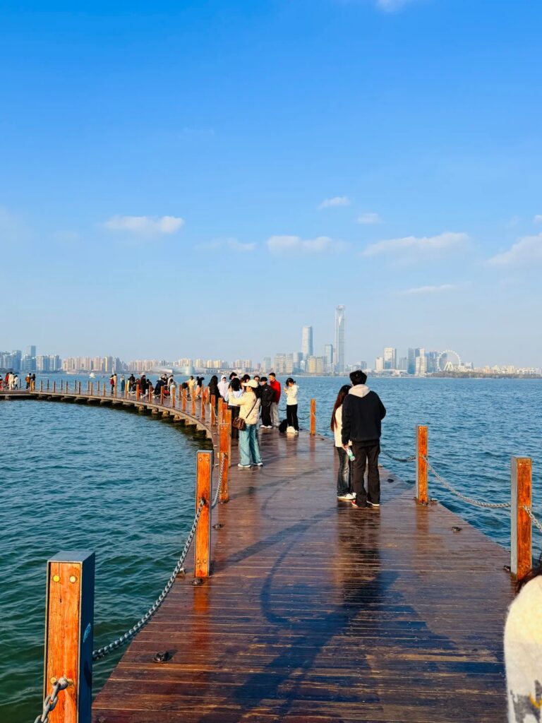 People on a wooden lakeside boardwalk with the Suzhou Industrial Park skyline beyond
