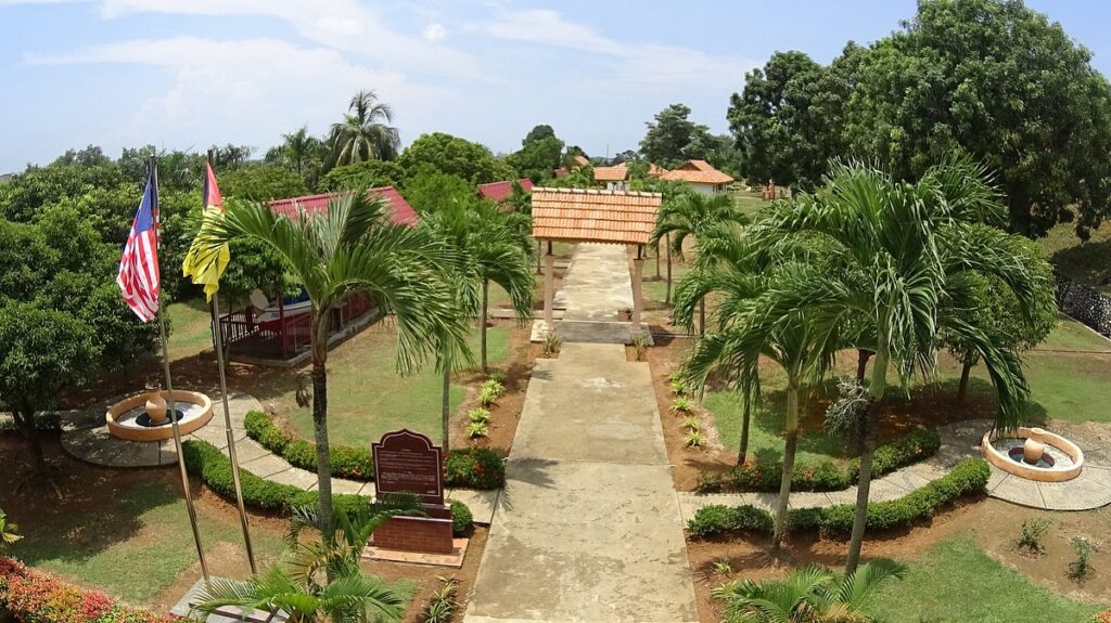 Landscaped grounds with a pathway, gazebo and Malaysian flags at Lukut Fort