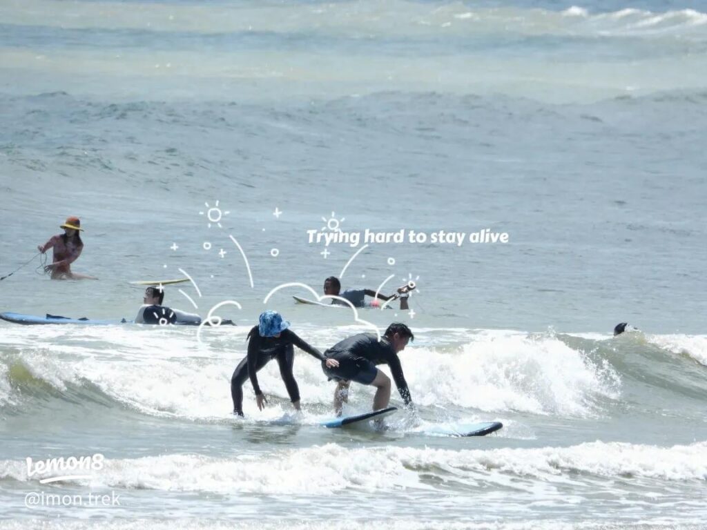 A learner riding a small wave on a foam board during a beginner surfing lesson at Desaru beach