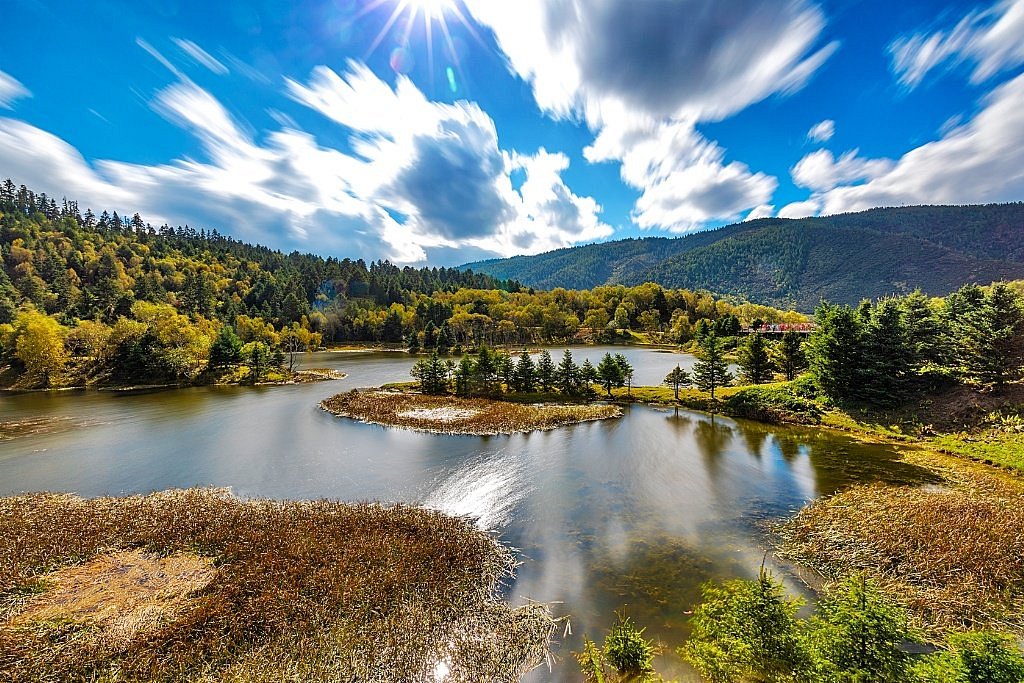 Alpine lake with wooded islets and grassland under a blue sky at Pudacuo National Park