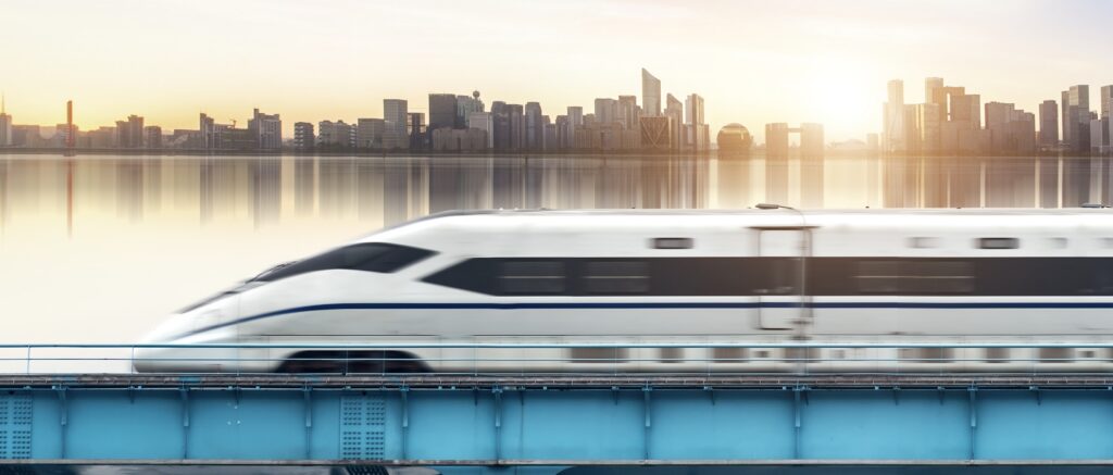 White high-speed train crossing a viaduct with a city skyline at sunset behind
