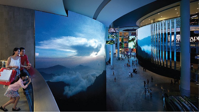 Visitors beside giant curved video screens inside SkyAvenue mall at Genting