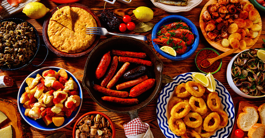 Overhead spread of Spanish tapas including patatas bravas, calamari, chorizo and olives
