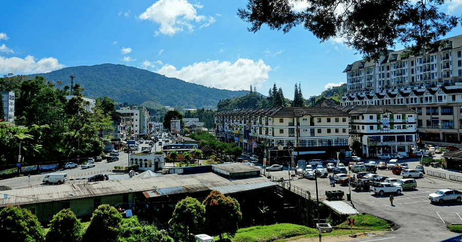 Cameron Highlands town centre with parked cars and shops below forested mountains