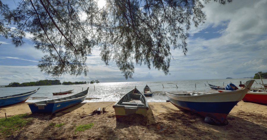 Traditional wooden fishing boats pulled up on a quiet Port Dickson beach under a tree