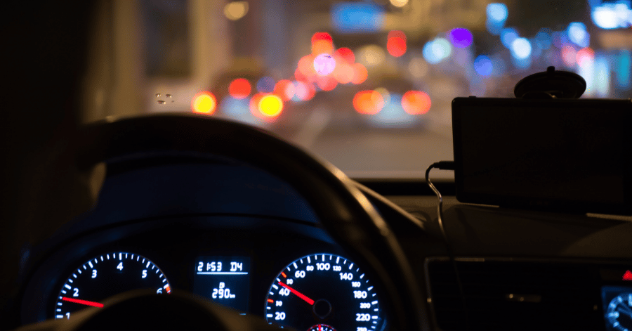 Driver's view of a lit car dashboard and blurred city lights while driving at night