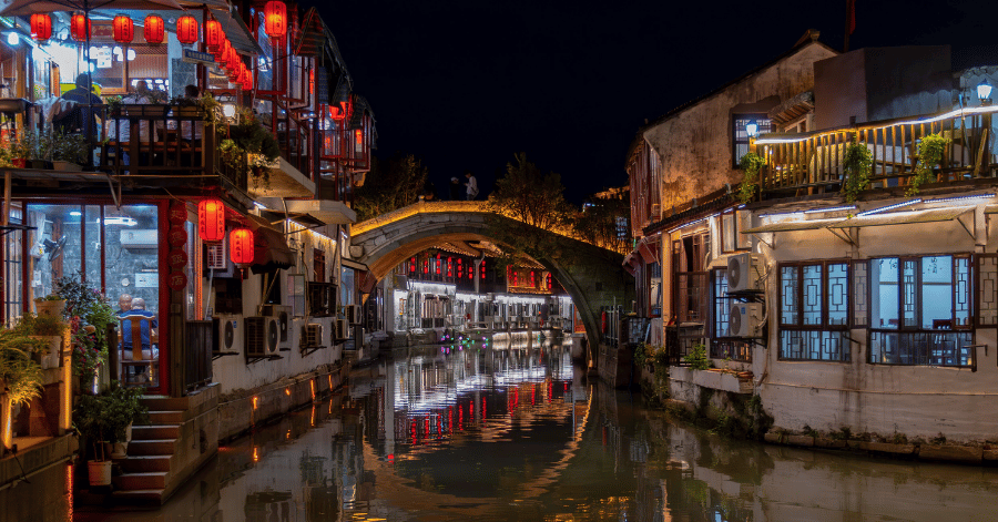 Lit shops and a stone arch bridge reflected in the canal at Shantang Street after dark