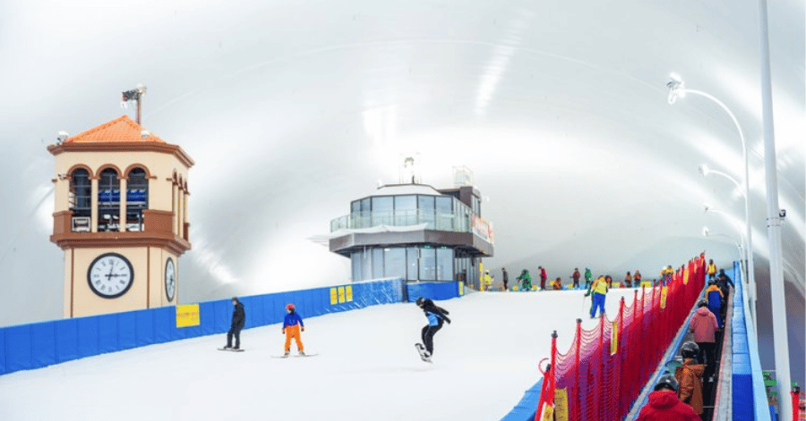 Skiers and snowboarders on an indoor snow slope beneath a domed roof