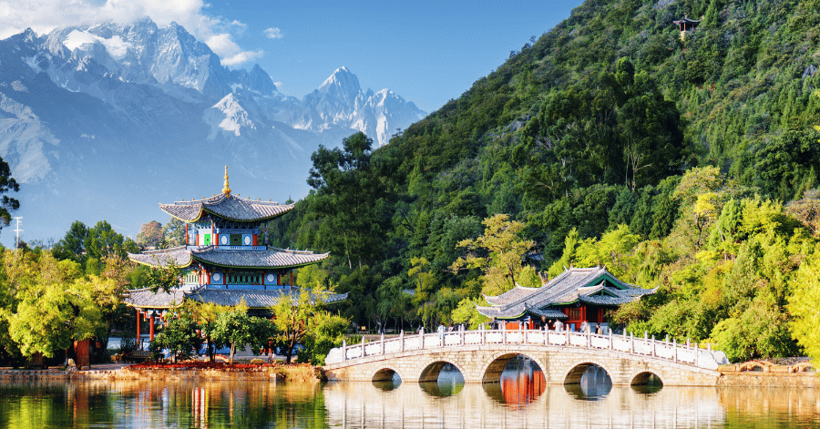 Lakeside pavilion and arched bridge below snow-capped mountains at Black Dragon Pool, Lijiang