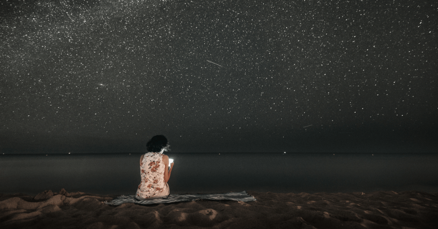 A person sitting on a beach at night under a sky full of stars