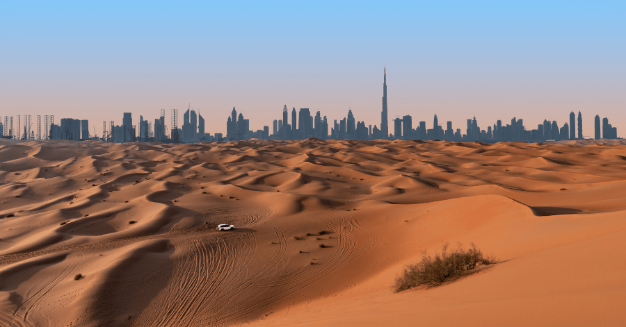 Dubai skyline with the Burj Khalifa rising beyond red desert dunes at dusk