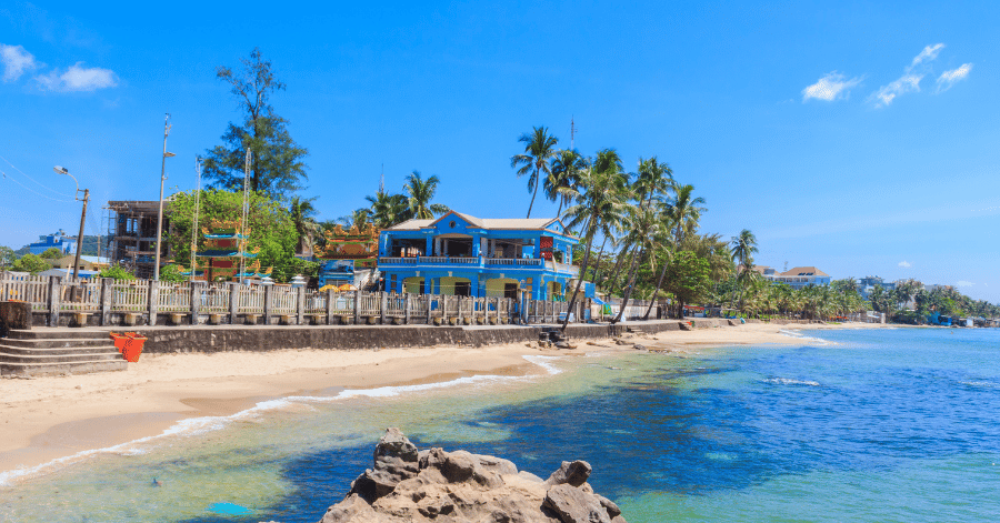 Sunny Phu Quoc beach with a blue beachfront cafe, palm trees and a rocky shore