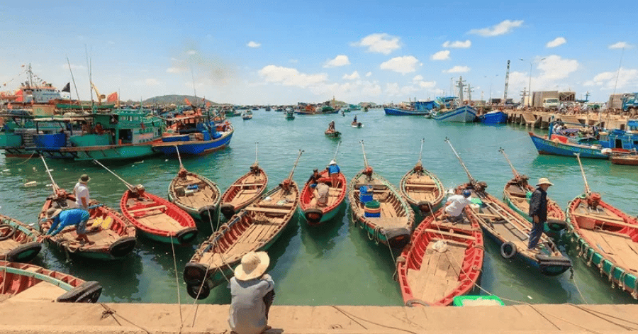 Wooden fishing boats moored at Ham Ninh village pier, a vendor in a conical hat in front