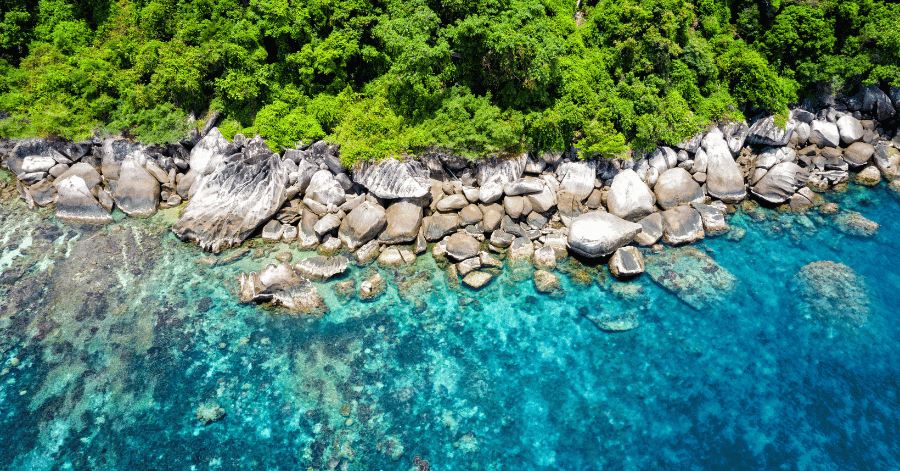 Aerial of granite boulders meeting clear turquoise water along Tioman's coast