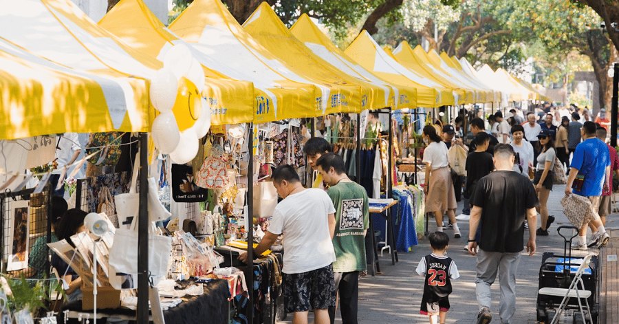 Shoppers browsing yellow-canopied stalls at an outdoor market in OCT Loft