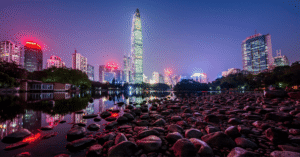 Shenzhen skyline at night with the lit Ping An tower reflected over water and pink flowers