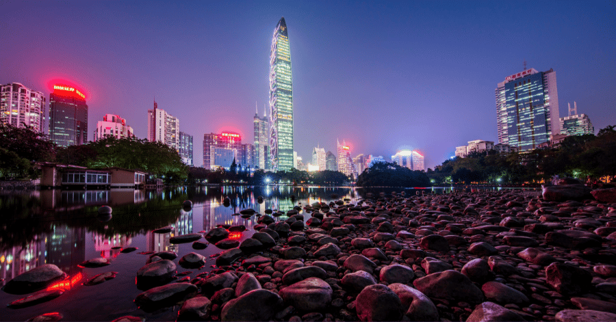 Shenzhen skyline at night with the lit Ping An tower reflected over water and pink flowers