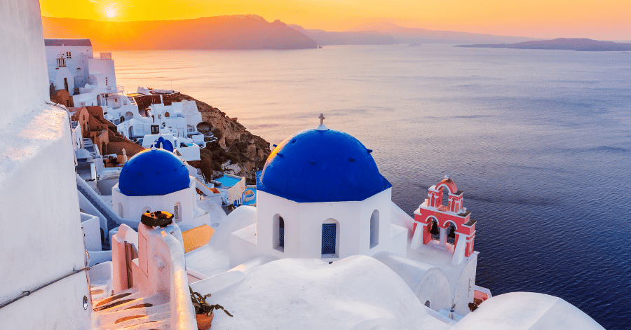 Whitewashed Oia churches with blue domes above the caldera at sunset, Santorini