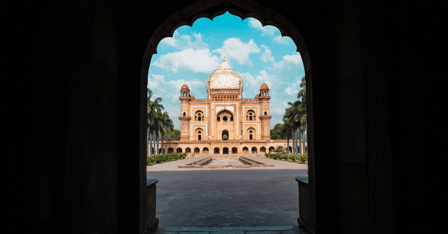 A domed Mughal sandstone mausoleum framed through a stone archway in India