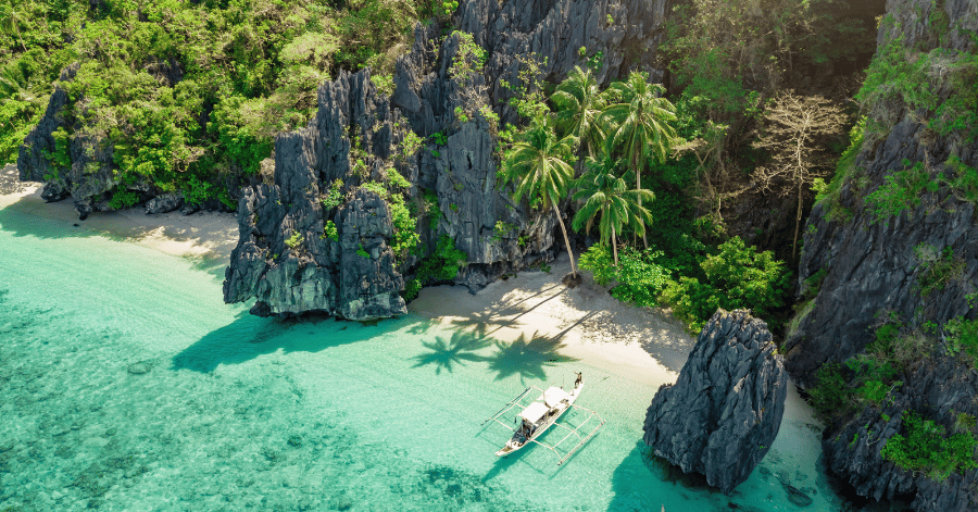 Turquoise hidden lagoon ringed by limestone karst cliffs with an outrigger boat, Palawan, Philippines
