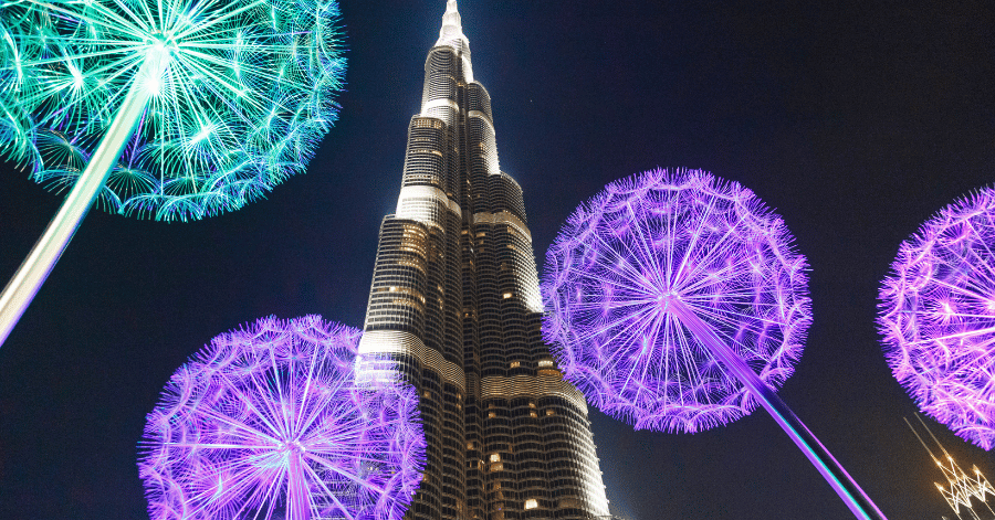 The Burj Khalifa lit up at night, framed by glowing purple dandelion-shaped light sculptures