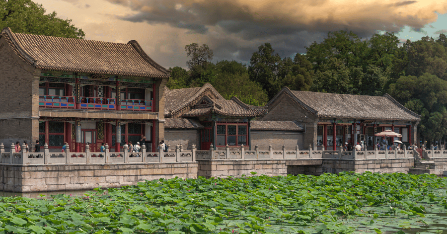 A traditional Chinese palace courtyard beside a lotus pond under cloudy skies