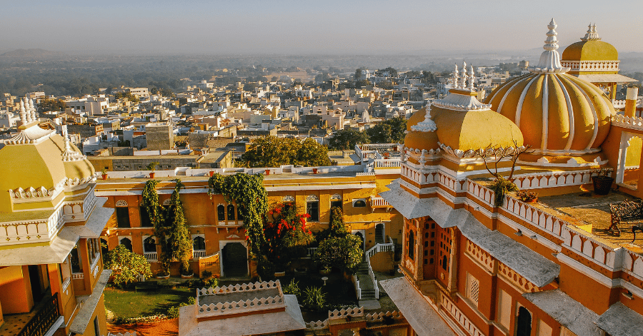 Aerial view of an ornate domed Indian palace overlooking a town under a hazy sky