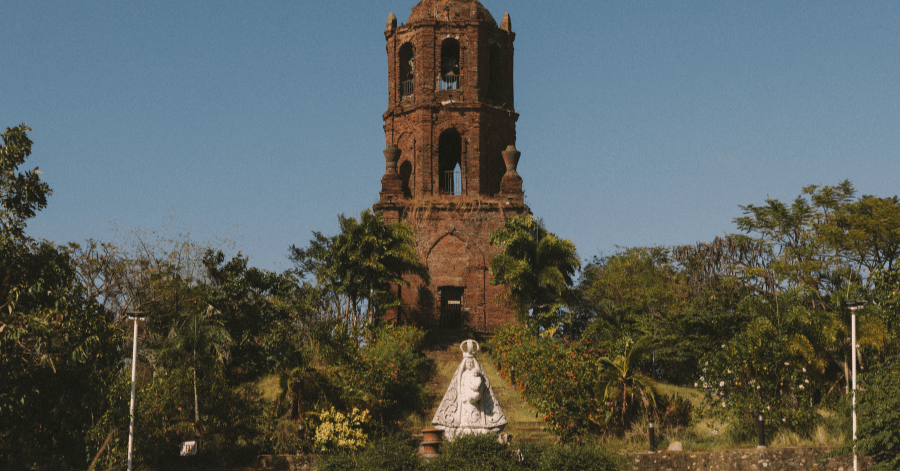 A historic Spanish-colonial stone bell tower in the Philippines under a clear blue sky