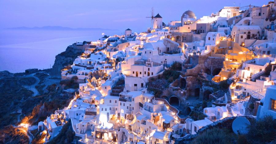 Oia's whitewashed houses lit up at blue-hour dusk along the caldera cliff, Santorini