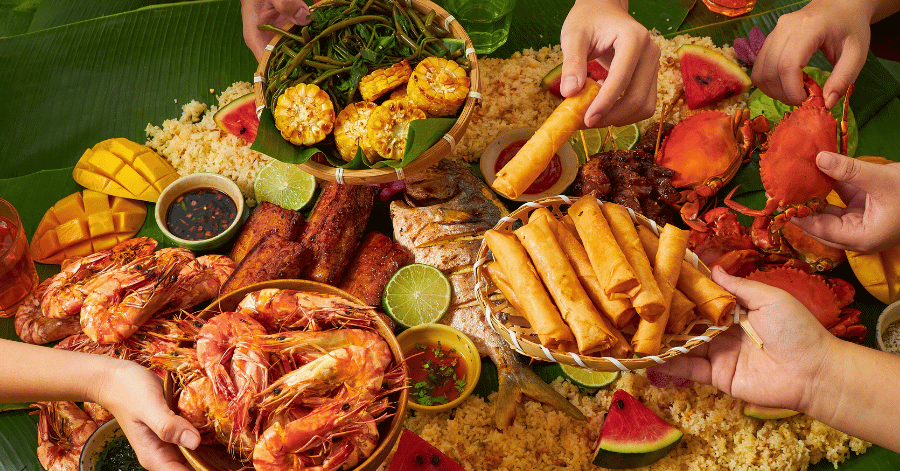 A shared Filipino boodle-fight feast of prawns, seafood, rice and lumpia, with hands reaching in