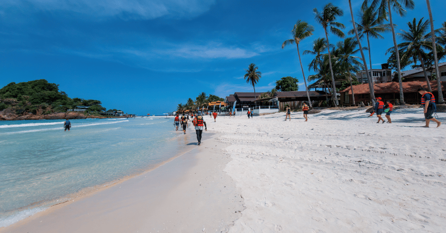 Visitors on the white sand of Redang's Long Beach with palm trees and resorts behind