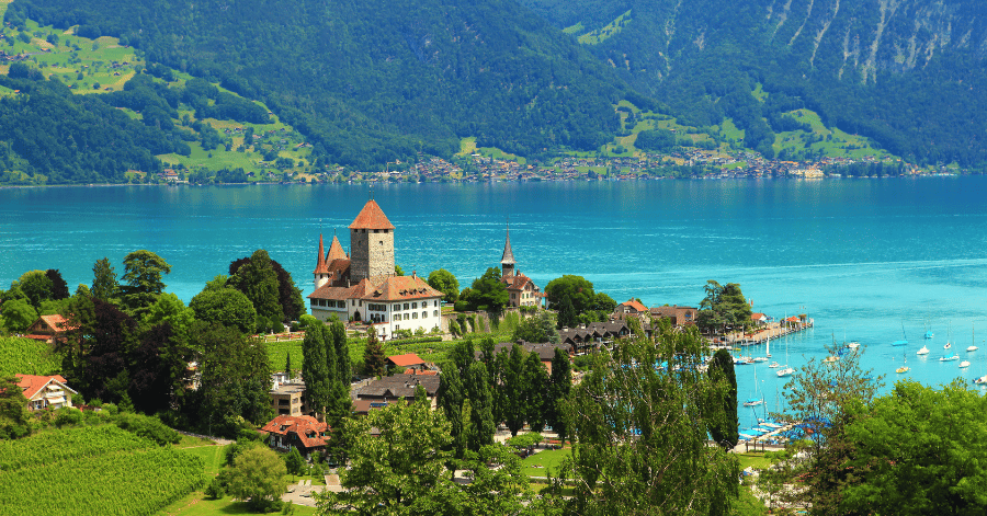 A turreted Swiss castle on the shore of a turquoise alpine lake, ringed by green hills
