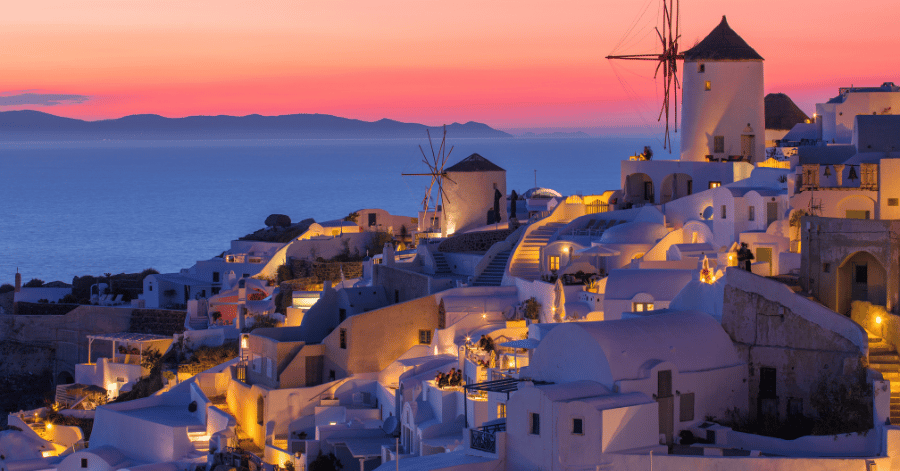 Oia's white windmills and houses silhouetted against a pink dusk sky over the sea